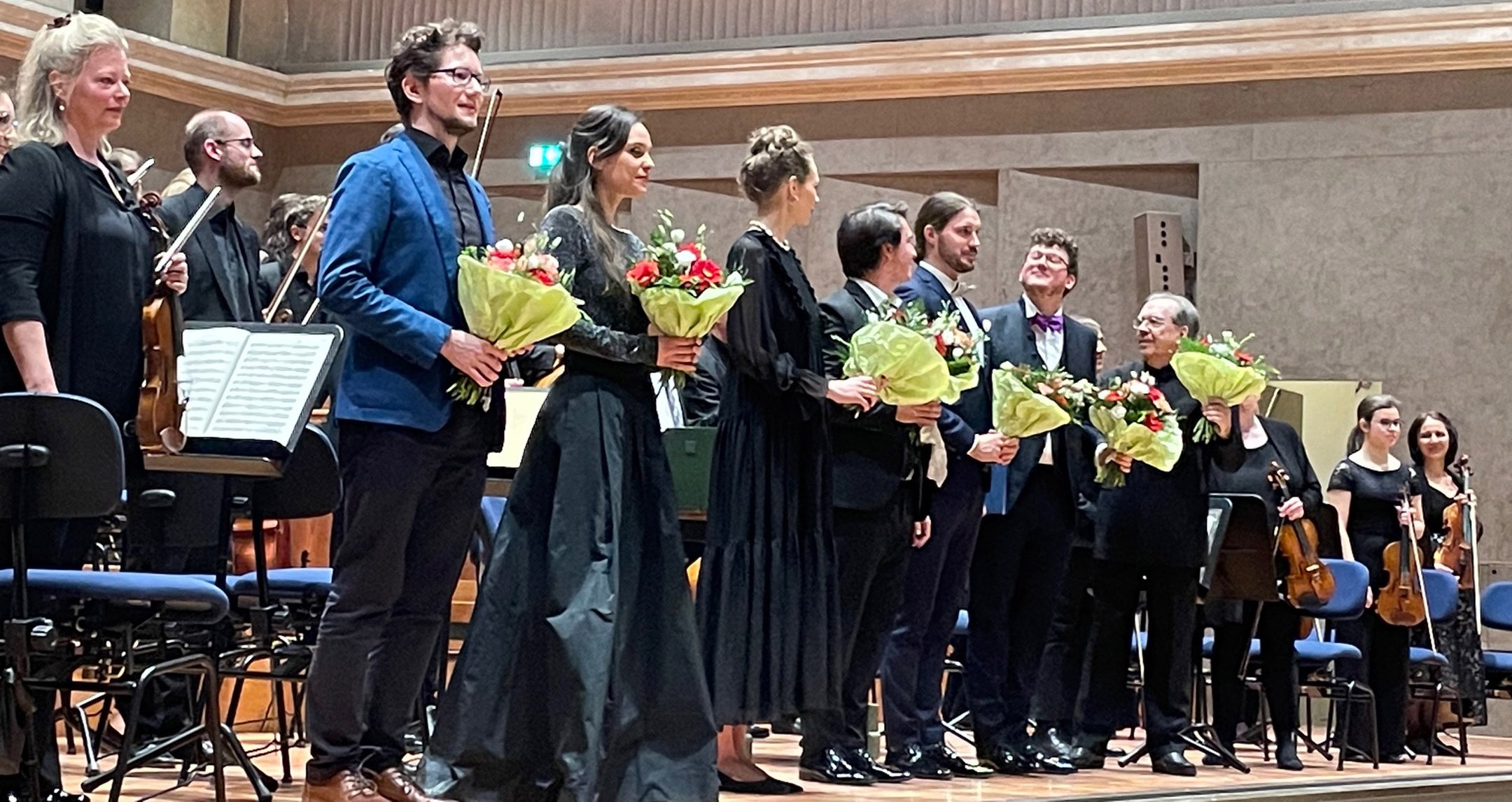 Künstler des Orchester stehen mit geschnekten Blumensträußen auf der Bühne