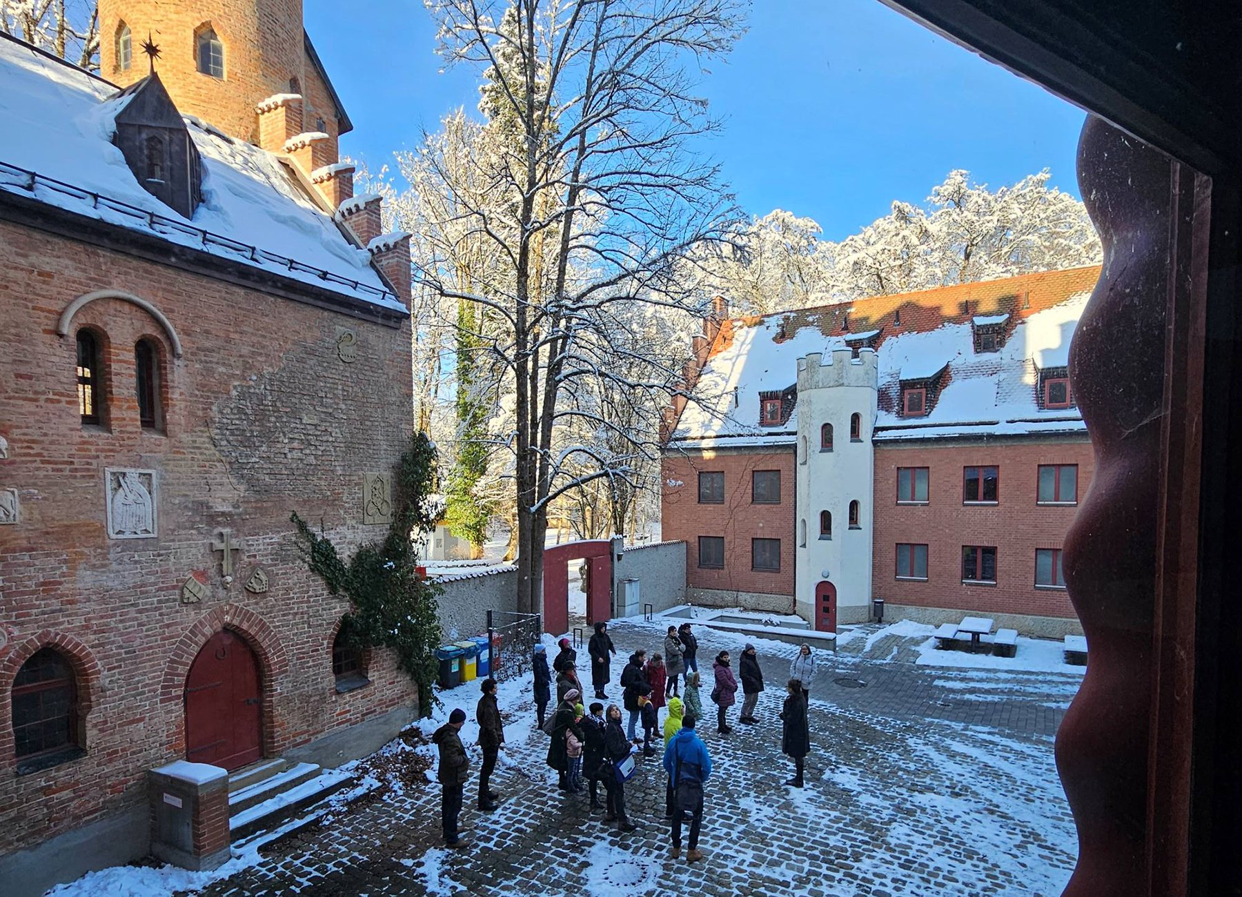 Eine Gruppe von Menschen versammelt sich auf einem schneebedeckten Burghof.