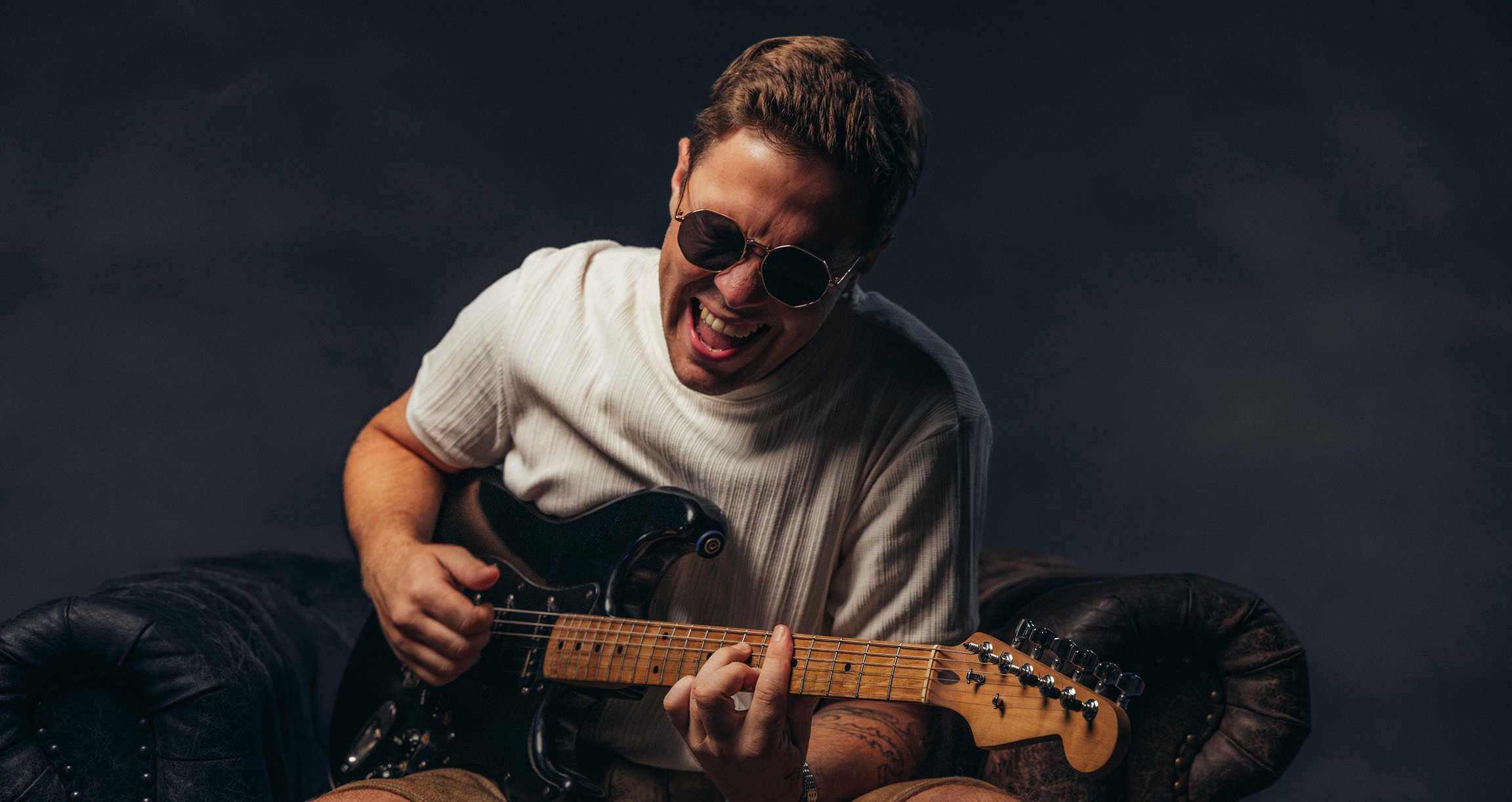 Ein Künstler mit Sonnenbrille spielt E-Gitarre und singt dabei 