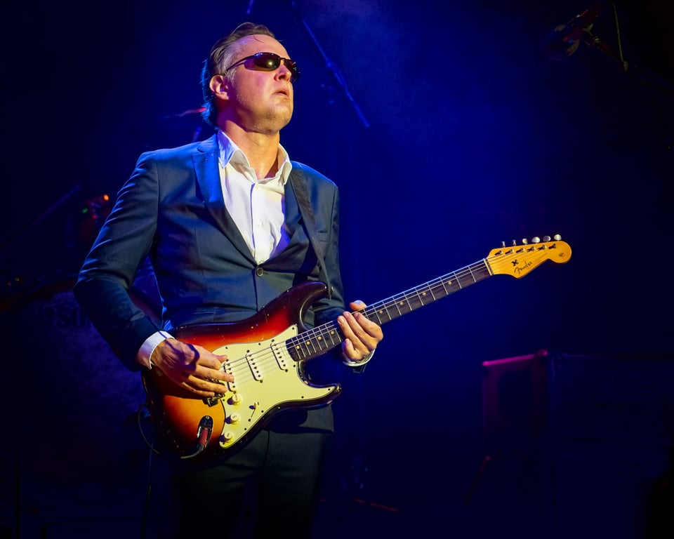 Joe Bonamassa steht im Anzug gekleidet auf der Bühne und spielt Gitarre.