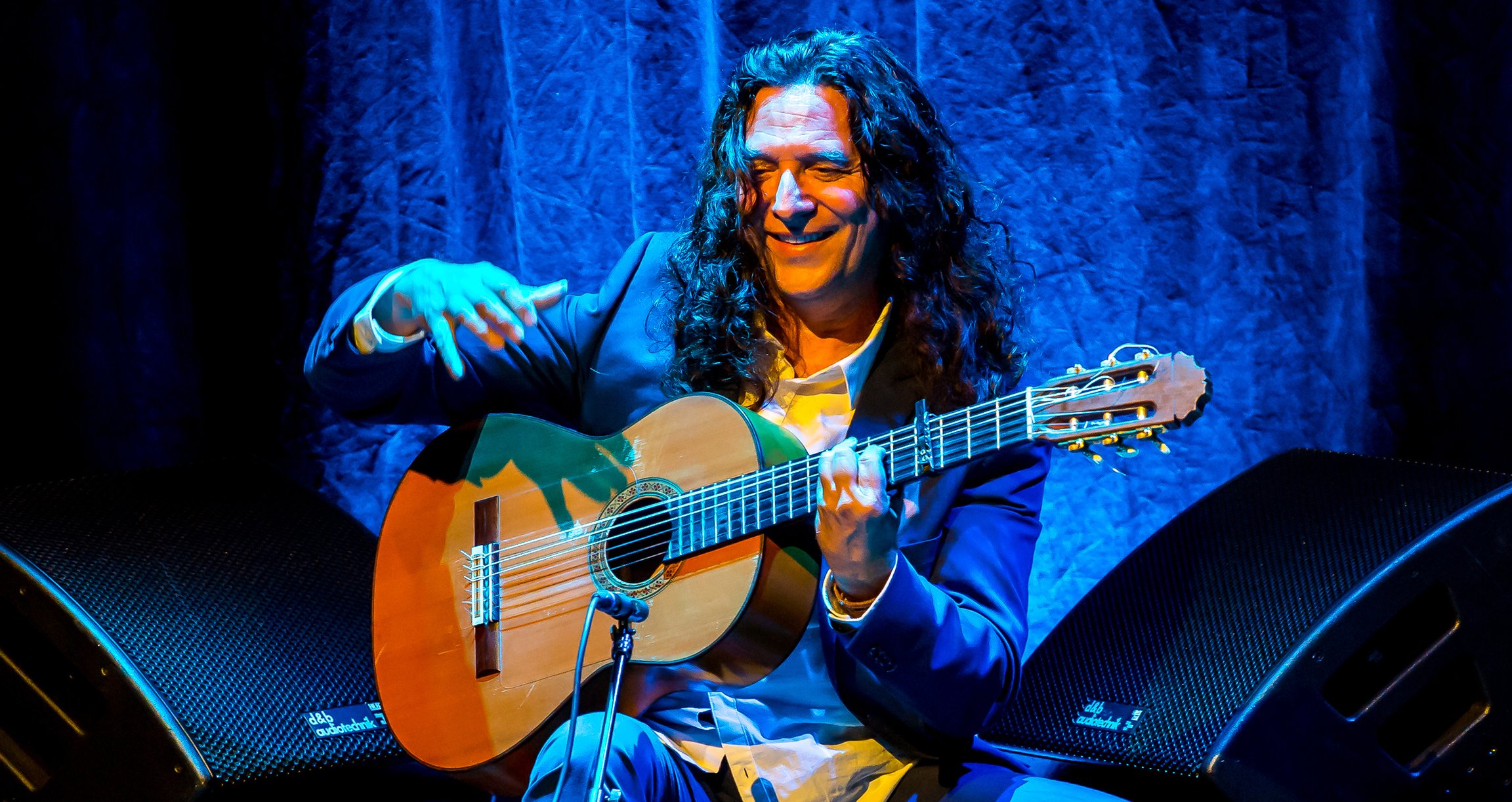 Ein Mann mit langen Haaren spielt voller Freude Gitarre.