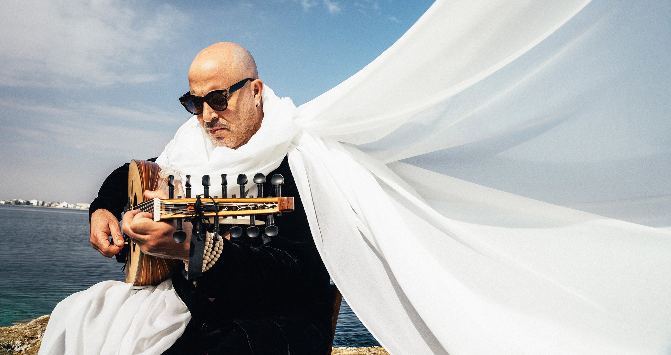 Ein Mann mit Sonnenbrille spielt am Meer Gitarre. 