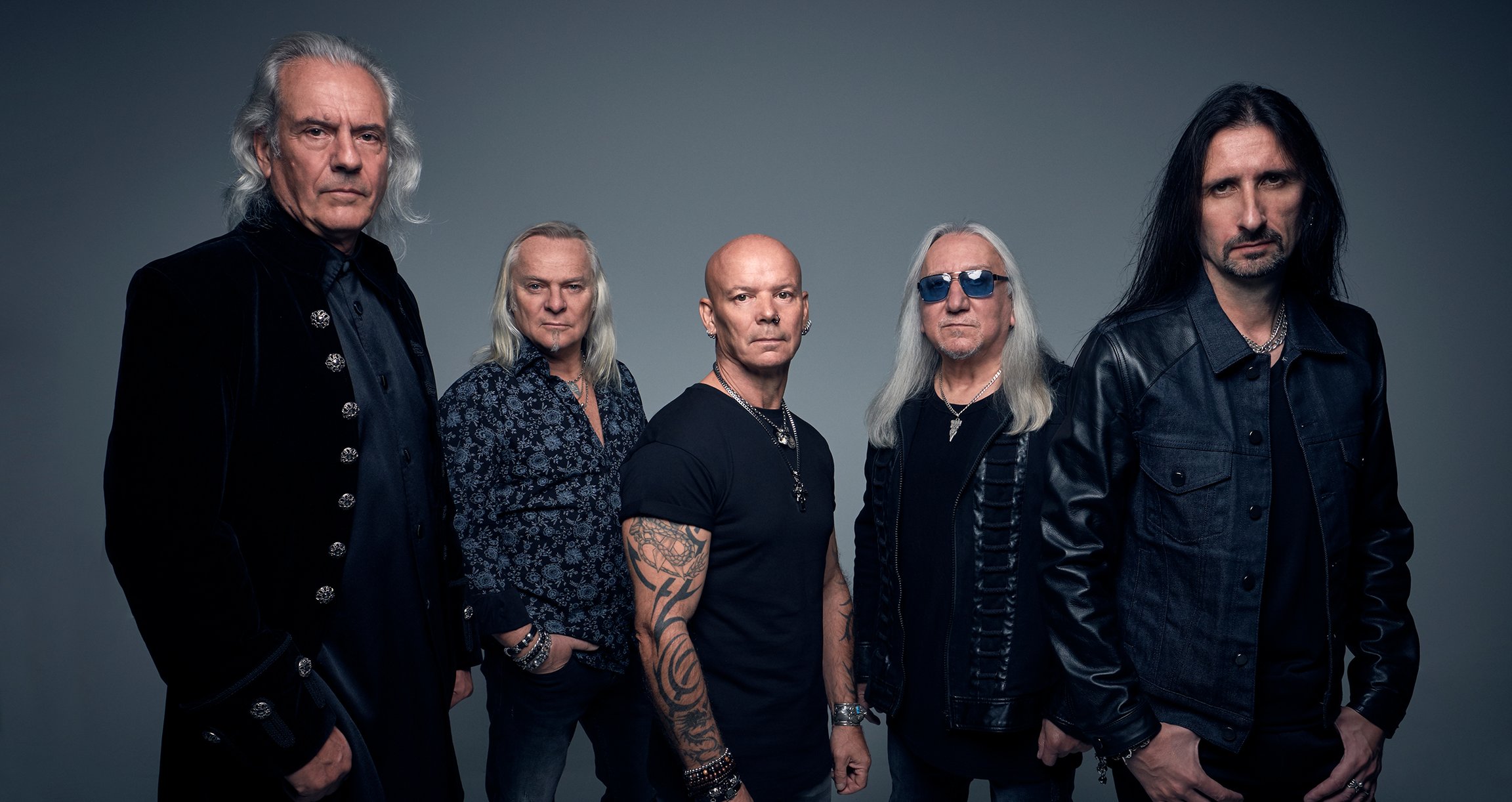 Uriah Heep steht vor einer dunklen Wand und macht ein Bandfoto