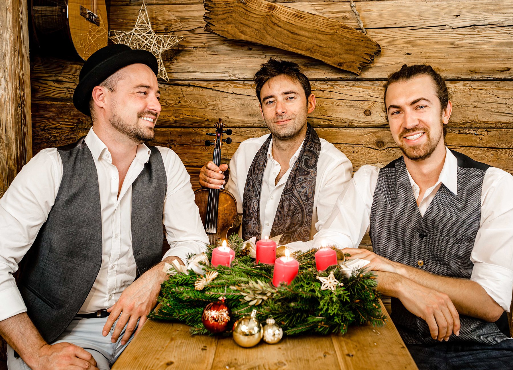 Cobario sitzen in formeller Kleidung an einem Tisch mit einem Adventskranz