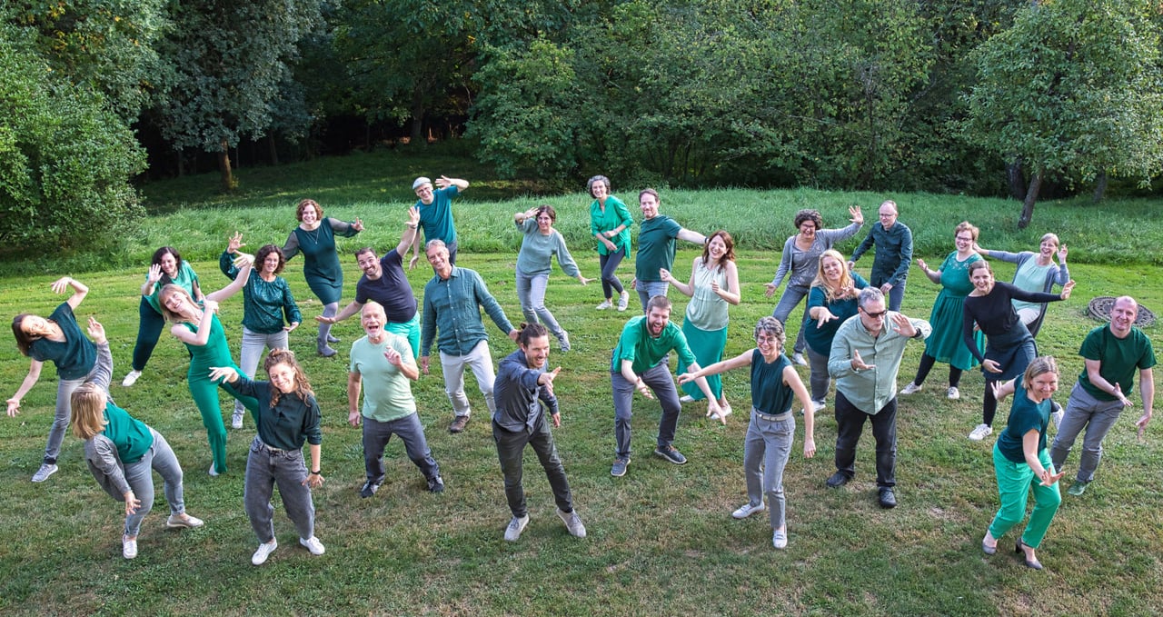 der Don Camillo Chor ist grün gekleidet. Sie stehen in dynamischer Pose auf Gras und werden von oben fotografiert