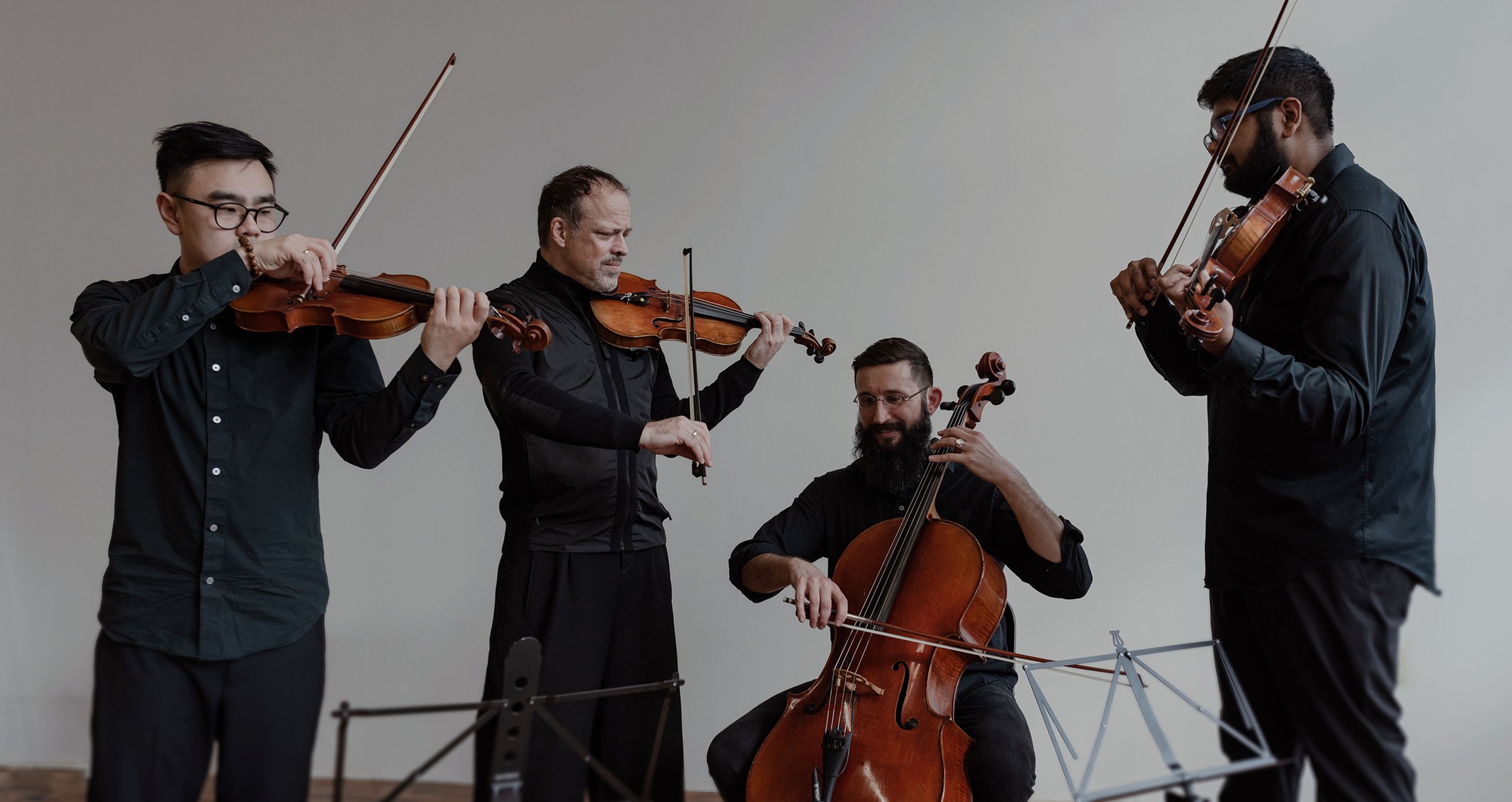 Vier Männer spielen in einem Raum Geige und Cello und schaffen eine harmonische musikalische Atmosphäre.